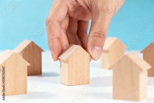 Hand placing wooden house model on blue background