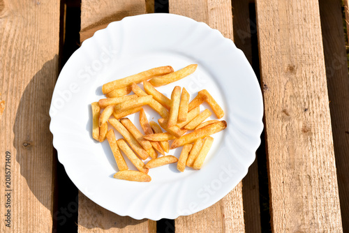 French fries on white plate on wooden background, junk food. 