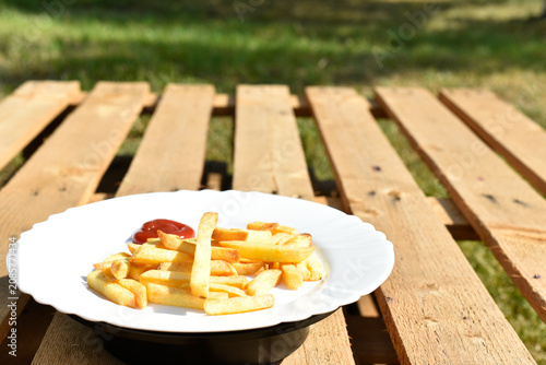 French fries on white plate on wooden background, junk food. 
