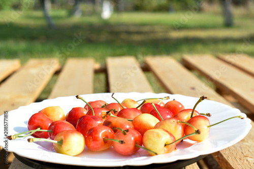 Ripe merry on white plate on wooden background, summer harvest 