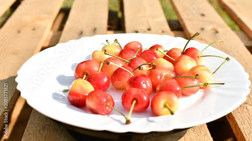 Ripe merry on white plate on wooden background, summer harvest 