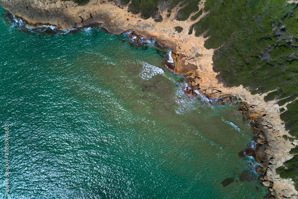Obraz premium Rugged rocky coast with vibrant turquoise water and green pine trees on the shore, perfect as a design template for summer travel.