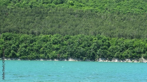 Lush green forest on steep hill above turquoise water of mountain lake. Concept of travel, ecology and pristine wilderness