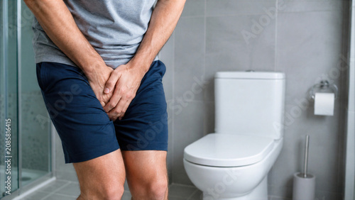 Man suffering from urgent need to urinate standing in bathroom holding crotch, medical problem or incontinence concept