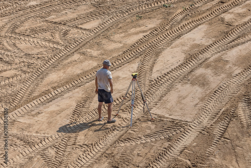 Surveyor with GNSS Receiver on Construction Site, Land Surveying and Site Measurement. Topographic measurements at a construction site. Aerial view of surveying equipment on sandy terrain.
