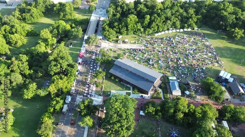 Visitors enjoy Independence Day activities across wide grass fields at Farmers Branch Historical Park. Mature tree canopy surrounds historic village architecture throughout Dallas Fort Worth, TX