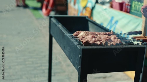 Raw meat skewers roasting on a black metal grill at an outdoor street fair. Cooked kebab on charcoal for catering event. Traditional street food preparation.