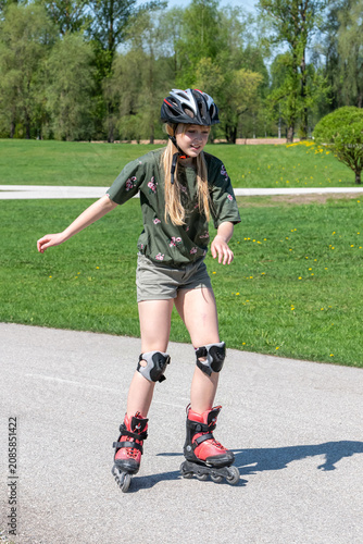 Foto Little girl with a helmet rollerskating in the park on a sunny summer day