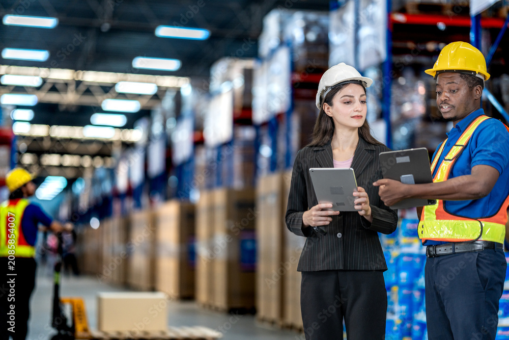 Fototapeta premium Industrial workers and manager coordinating storage and logistics in a modern facility. Efficient team utilizing technology and manual handling for effective warehouse management.
