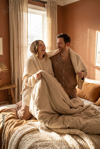 Couple laughing while making the bed together in a cozy bedroom  