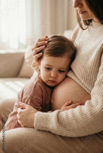 Young child embracing pregnant woman's belly while sitting on sofa  