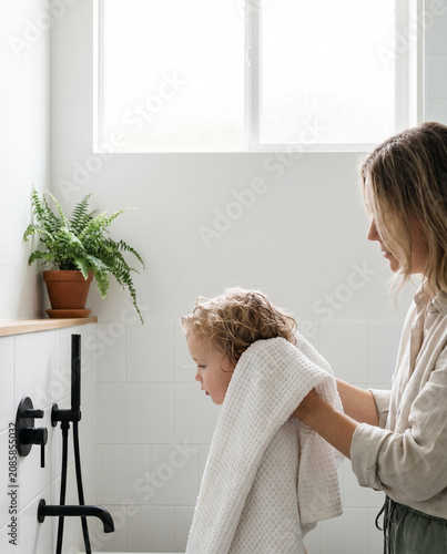 Mother drying child's hair with towel in bright bathroom setting  