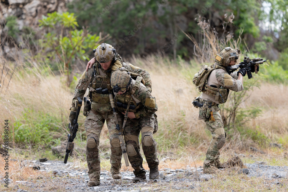Fototapeta premium Soldier carries injured comrade over rocky terrain