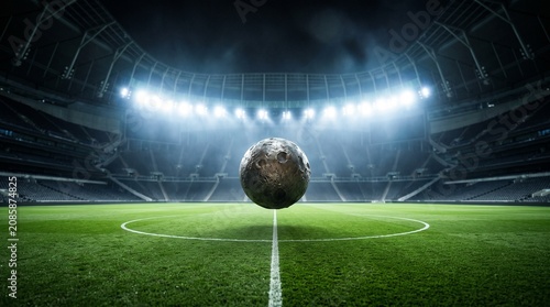 Surreal scene of the moon hovering over a football stadium pitch at night under bright stadium lights