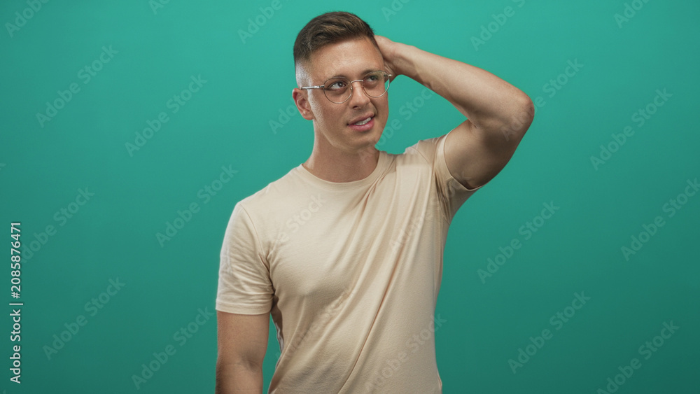 Fototapeta premium Man with hand on head, wearing glasses and beige tee, exposed forearm visible against studio backdrop; calm reflection.