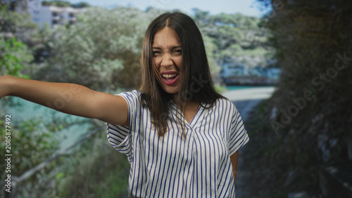 фотографія Woman with arms crossed in forest, striped shirt visible, pursing lips and squinting at camera with folded arms; stubborn defiance