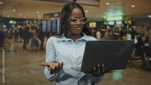 Schilderij op canvas Woman holding laptop, typing and frowning while checking screen near departure boards in airport terminal; frustration problem solving