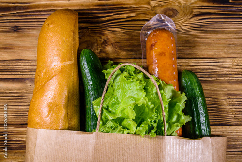 Paper bag with different food from grocery on a wooden table. Supermarket shopping concept. Top view