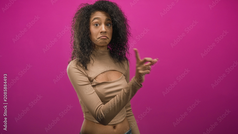 Obraz premium Woman points finger toward camera showing bare navel and midriff in pink studio backdrop; skepticism playfulness.