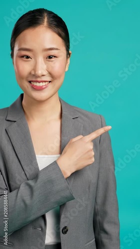 Diverse professional smiling confidently in a contemporary outfit, pointing left against a vibrant teal background with copy space. Subtle dolly in video, bright studio lighting, concept of clear