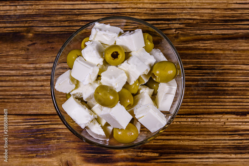 Chopped feta cheese and olives in glass bowl on a wooden table. Top view
