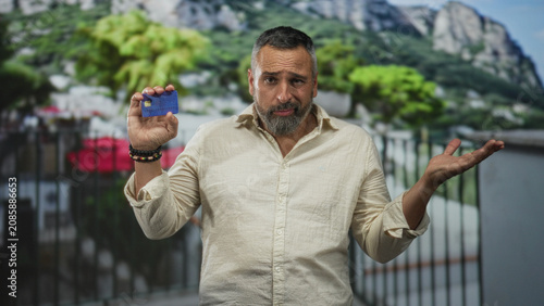 Принти на полотні Man holding creditcard, shrugging on building balcony with raised hand and palm up; payment doubt confusion