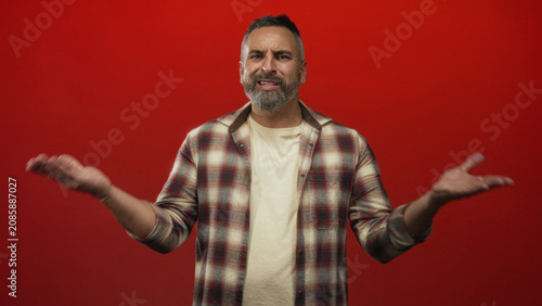 Obraz na plátně Man showing hands raised, pointing finger and open palms in red studio; frustration warning admonition stern