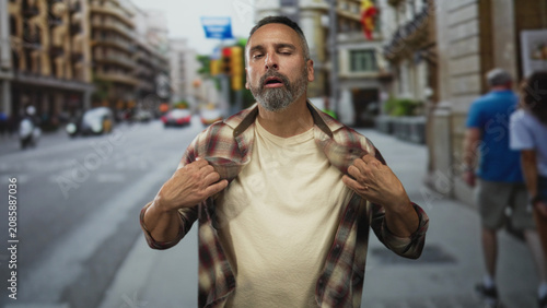 Tableau sur toile Man with beard and grey hair pulling open flannel shirt on urban street, eyes closed and hands gripping collar in broad gesture; relief