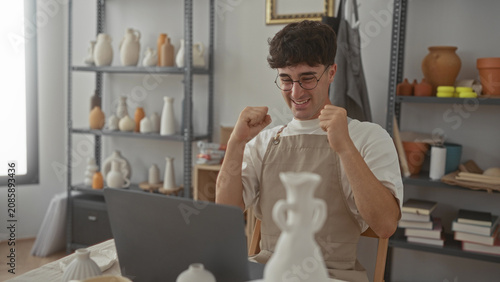 Man typing on laptop in studio surrounded by pottery and shelves, hands on keyboard showing concentration; creative satisfaction.