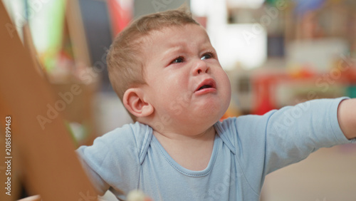 Foto Toddler boy crying with open mouth, tears and outstretched arm reaching for a toy handle in a building play area; distress need
