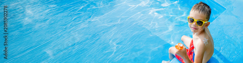Cute boy in sunglasses with sunscreen lotion on shoulder by swimming pool.