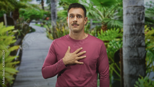 Foto Hispanic man with mustache, hand on chest on boardwalk path, wearing maroon long sleeve shirt and looking earnest; sincerity gratitude