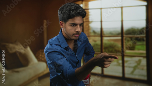 Fotografija Man reporter in blue shirt pointing finger to camera with red news microphone, right hand out and left hand on hip in studio; assertive reporting