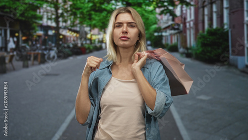 Slika na platnu Woman carrying shopping bag on shoulder, hand adjusting strap while looking annoyed in street; annoyance independence