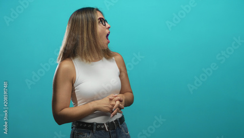 Valokuva Woman with raised hands and open mouth showing surprise in studio with turquoise backdrop, white sleeveless top and jeans; celebration excitement