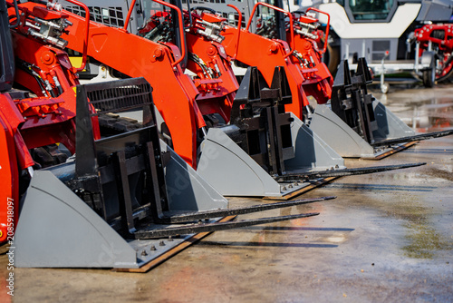 Fotografie A row of new red skid steer loaders equipped with industrial pallet forks parked