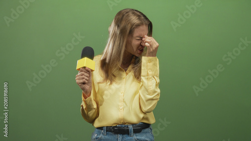 Obraz na plátně Reporter woman holding microphone pinches bridge of nose and closes eyes in studio signaling pause and discomfort; frustration