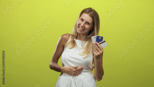 Blonde woman holds creditcards fanned in one hand while other hand rests on her stomach in a studio setting; financial joy.