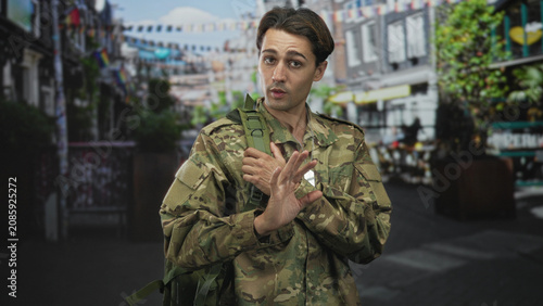 Tableau sur toile Man soldier in camouflage uniform touching dogtag and making ok sign with right hand while carrying backpack on street; duty resolve hope