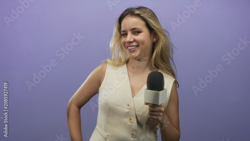 Canvastavla Woman reporter holding handheld microphone in studio with purple backdrop, blonde smiling while presenting with hand on hip; friendly confidence