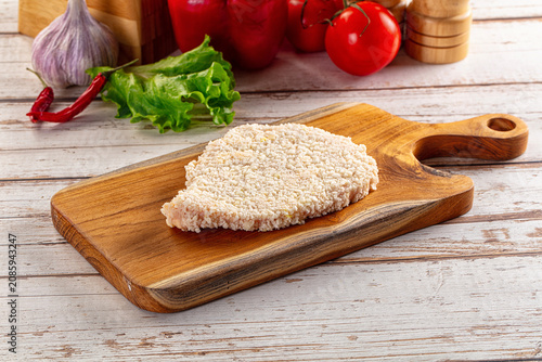 Breaded chicken cutlet on wooden cutting board with fresh vegetables