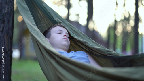 A young boy sleeps peacefully in a green hammock among forest trees. Serene outdoor relaxation and nap in soft daylight 