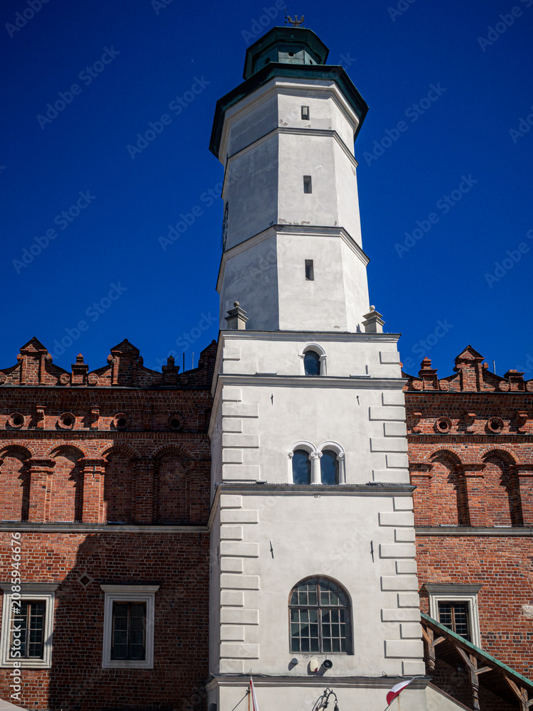 Fototapeta premium Historic white tower and red brick building under clear blue sky