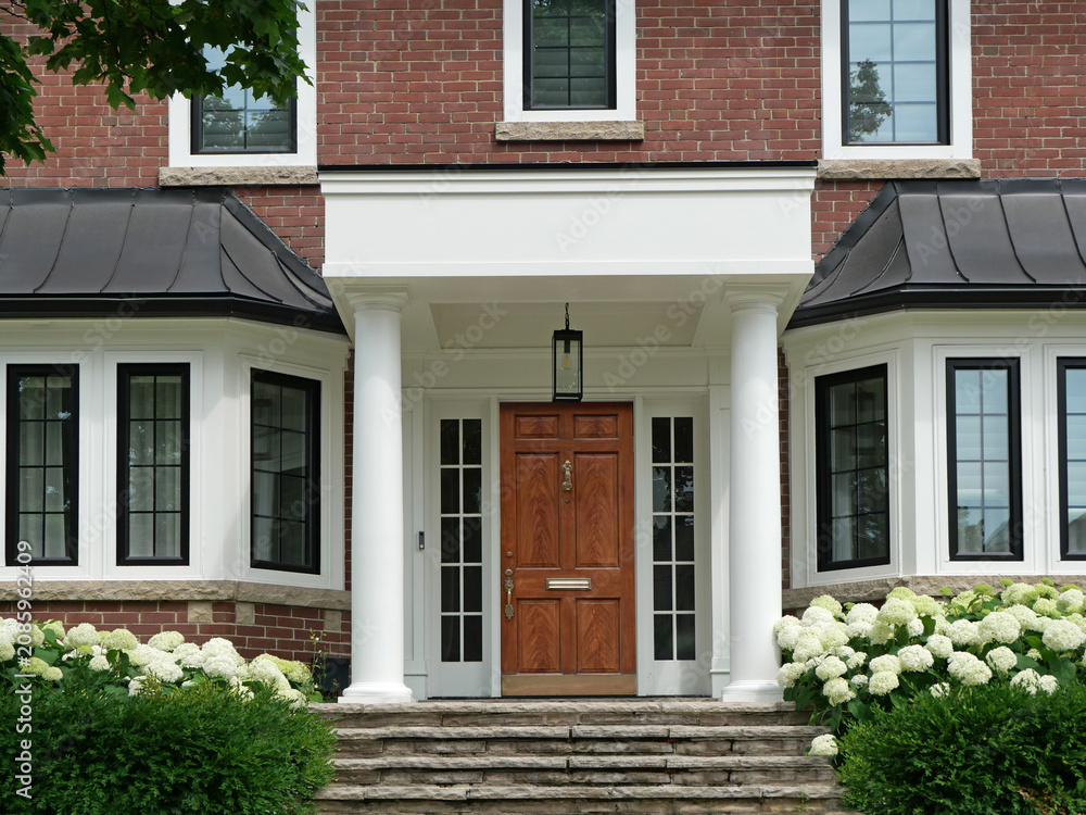 Obraz premium Traditional brick two story house with portico entrance and elegant wood grain front door