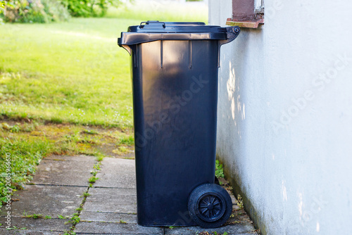 Cuadro en lienzo Black wheelie bin standing by the house wall for residual household waste disposal