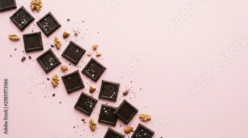 Dark chocolate squares with walnuts and almonds on a light pink background