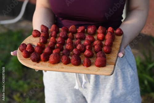 Fotografía Front close-up view of a young woman holding a wooden cutting board filled with freshly washed ripe strawberries