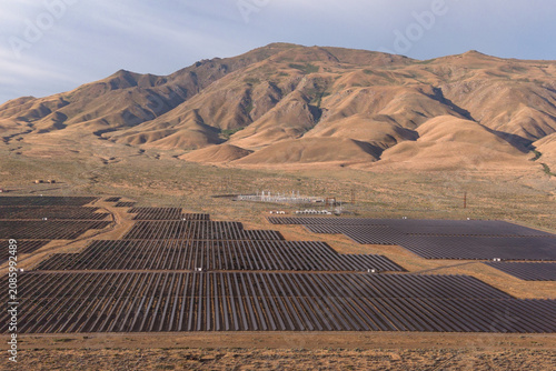 A utility-scale solar farm spreads across the northern Nevada high desert, with dramatic barren hills rising steeply in the background.