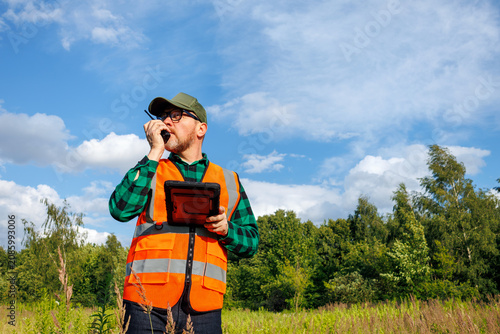 Bild auf Leinwand Climatologist or ecologist holding a digital tablet and talking on a walkie-talkie while monitoring the environmental effects of global warming and climate change in a summer field