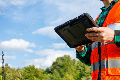 Photography Close-up of an ecologist or meteorologist holding a rugged digital tablet while conducting outdoor research on climate change during a hot summer day